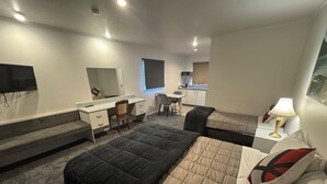 A hotel room with a bed, a desk, a chair, a small kitchenette, and a TV. - Settlers Motor Lodge (Lower Hutt)