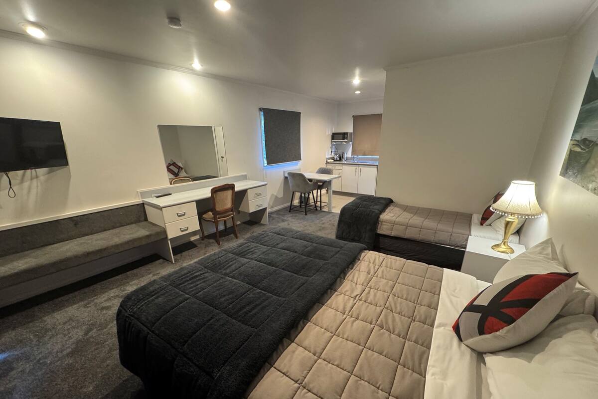 Ein Hotelzimmer mit Bett, Schreibtisch, Stuhl, einer kleinen Küchenzeile und einem Fernseher.
