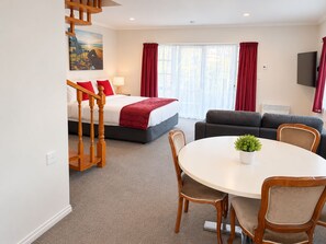 A hotel room with a bed, a sofa, a dining table with chairs, a staircase, and a painting on the wall. - Settlers Motor Lodge (Lower Hutt)
