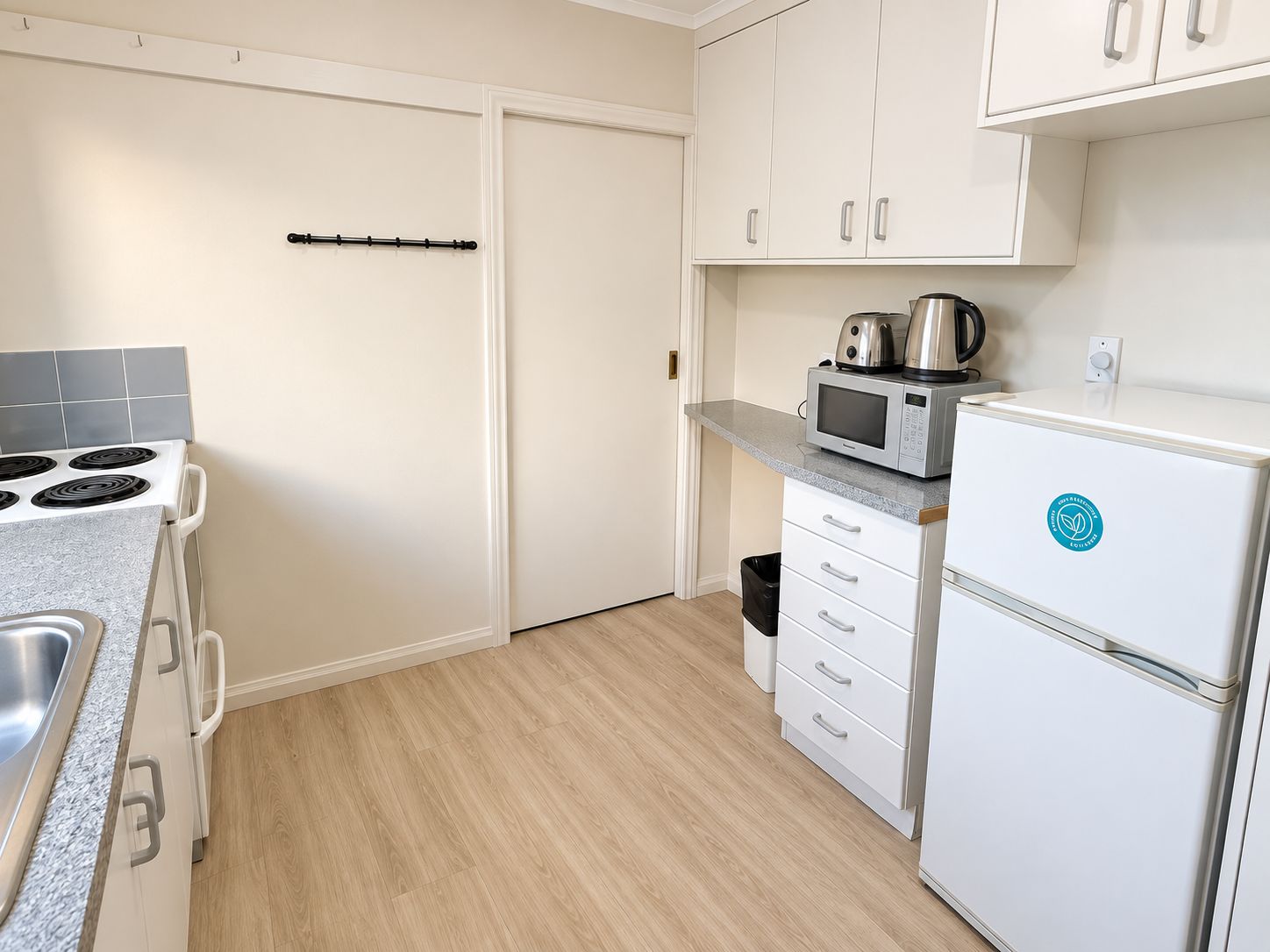 Cocina compacta con estufa, microondas y refrigerador, con armarios blancos y salpicadero de azulejos.
