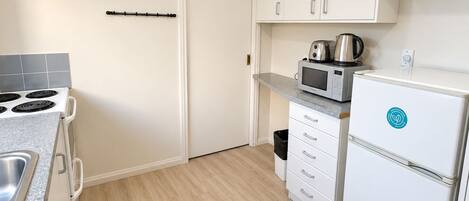A compact kitchen with a stove, microwave, and refrigerator, featuring white cabinetry and a tiled backsplash.