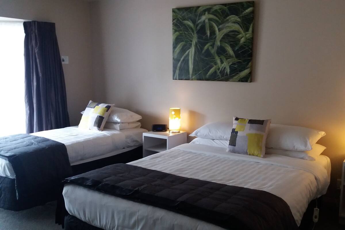 Ein Hotelzimmer mit zwei Betten, Nachttischen, Lampen, einem Gemälde und einem Fenster mit Vorhängen.