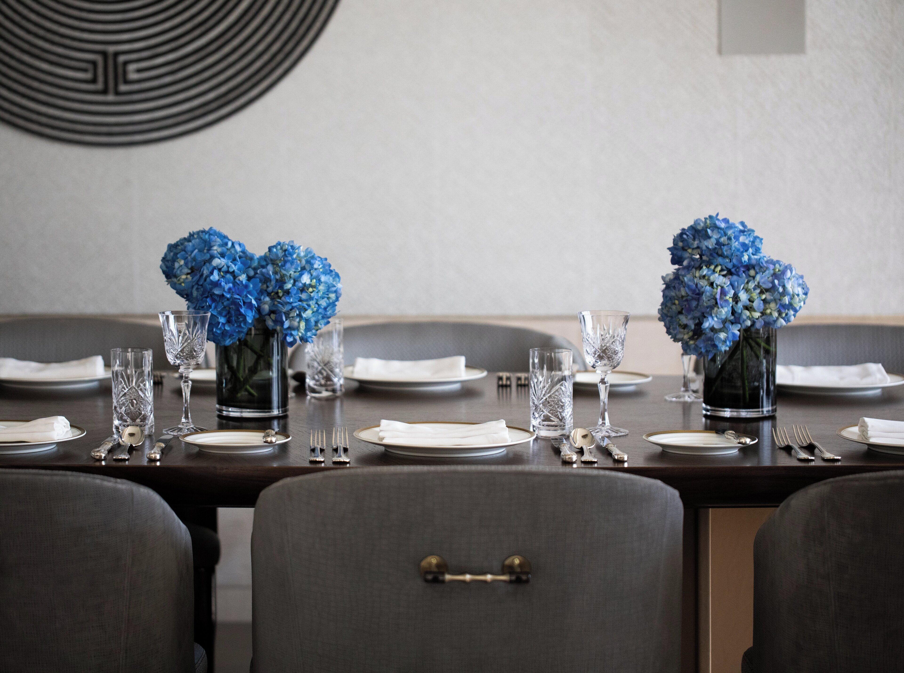 A dining table set with blue flowers, clear glassware, and silverware.