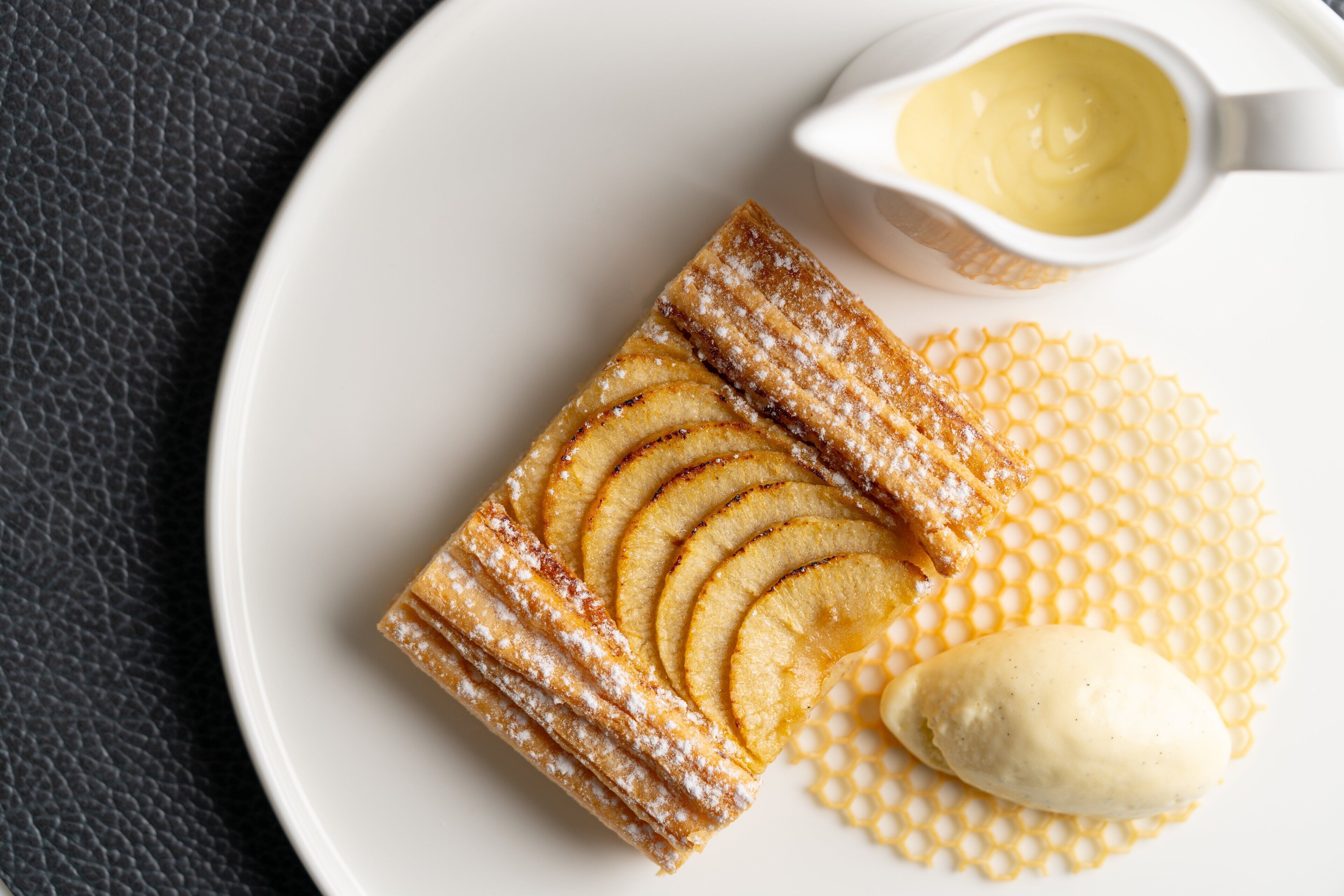 A dessert plate with a pastry, apple slices, and a scoop of ice cream.