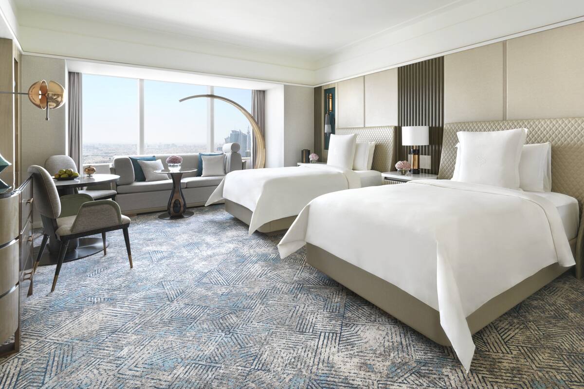 Habitación de hotel con dos camas, un sofá, una mesa de comedor y vista a la ciudad.