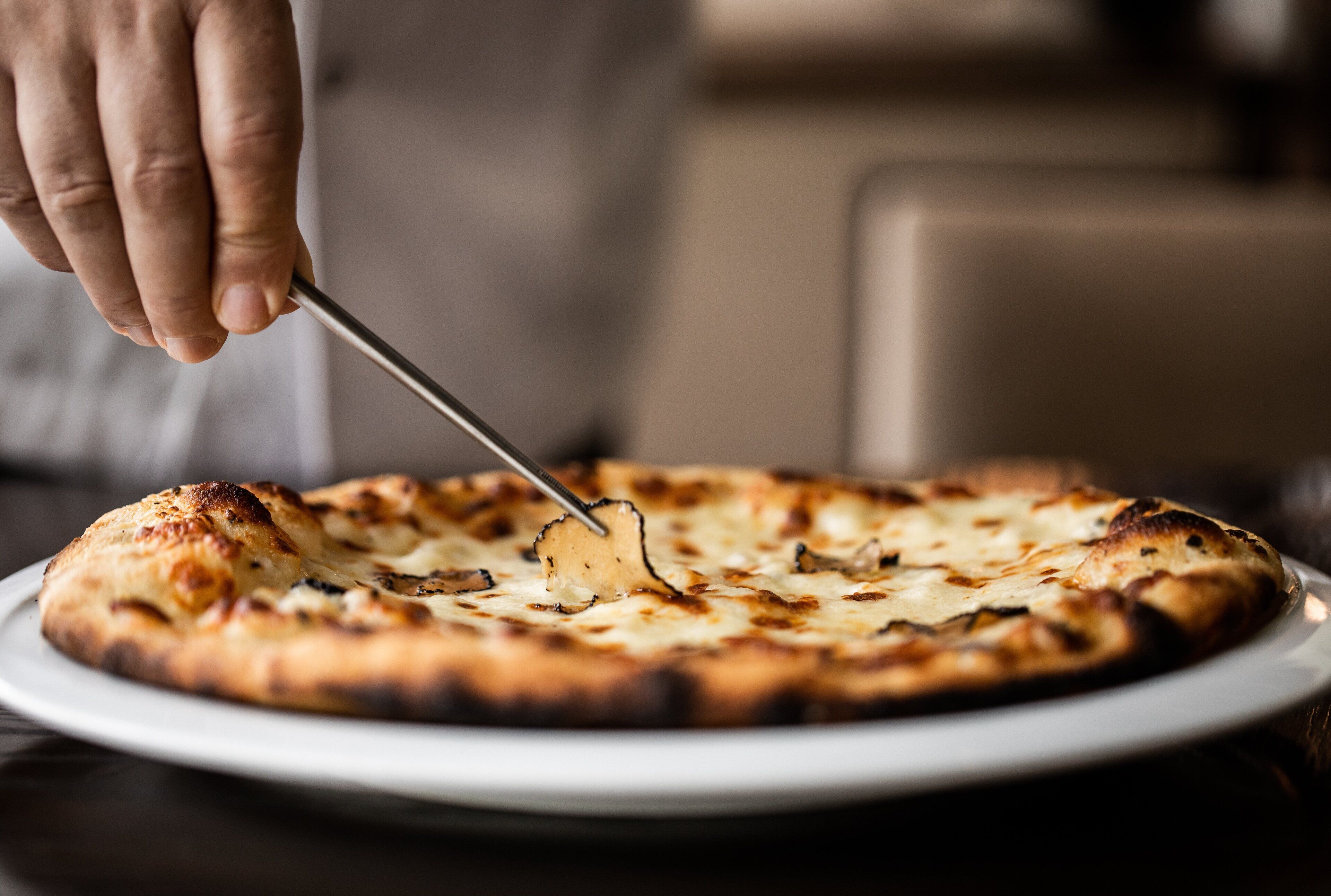 Une main utilise un coupe-pizza pour découper une pizza sur une assiette blanche.