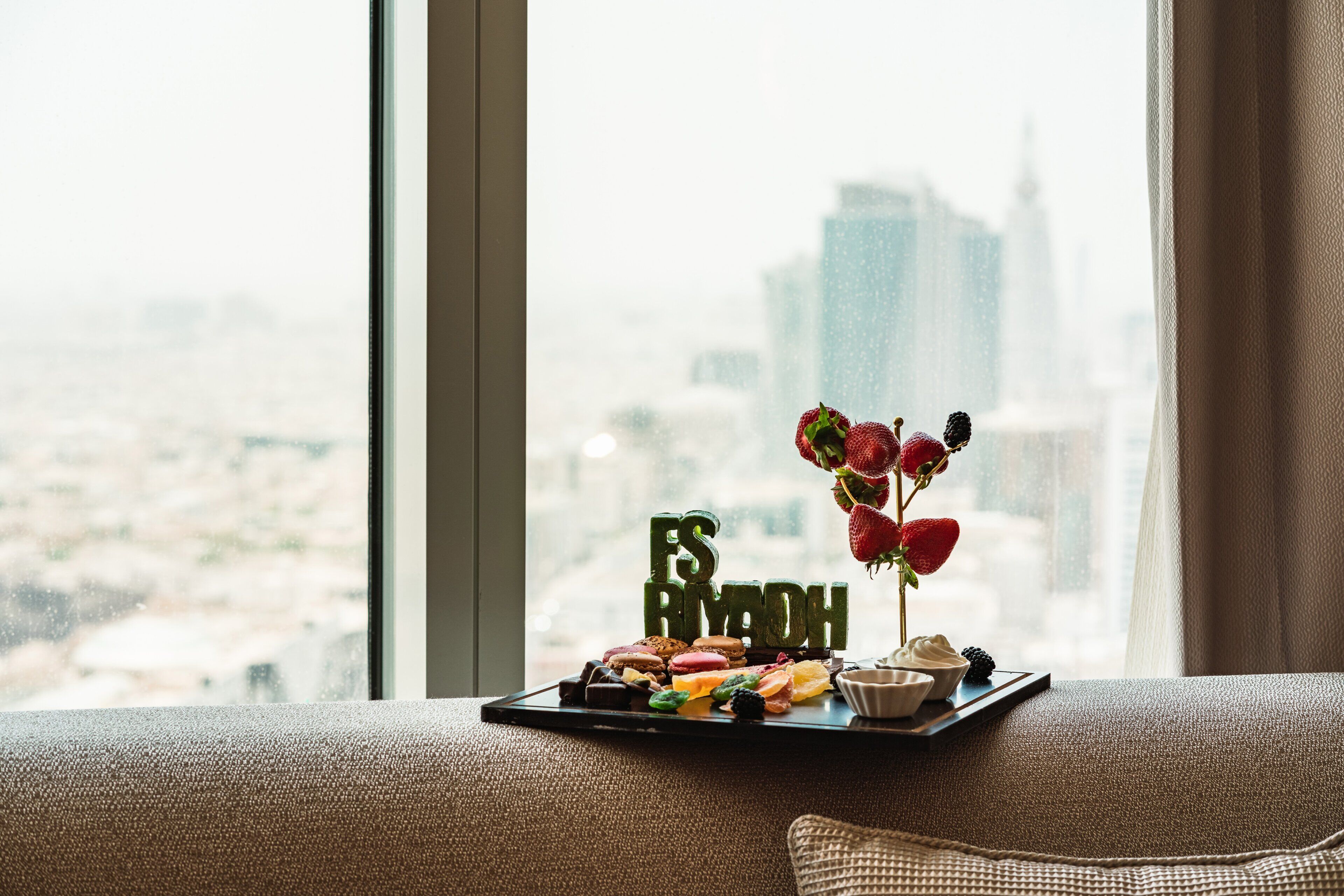 A tray of assorted pastries and a floral arrangement on a windowsill with a cityscape view.