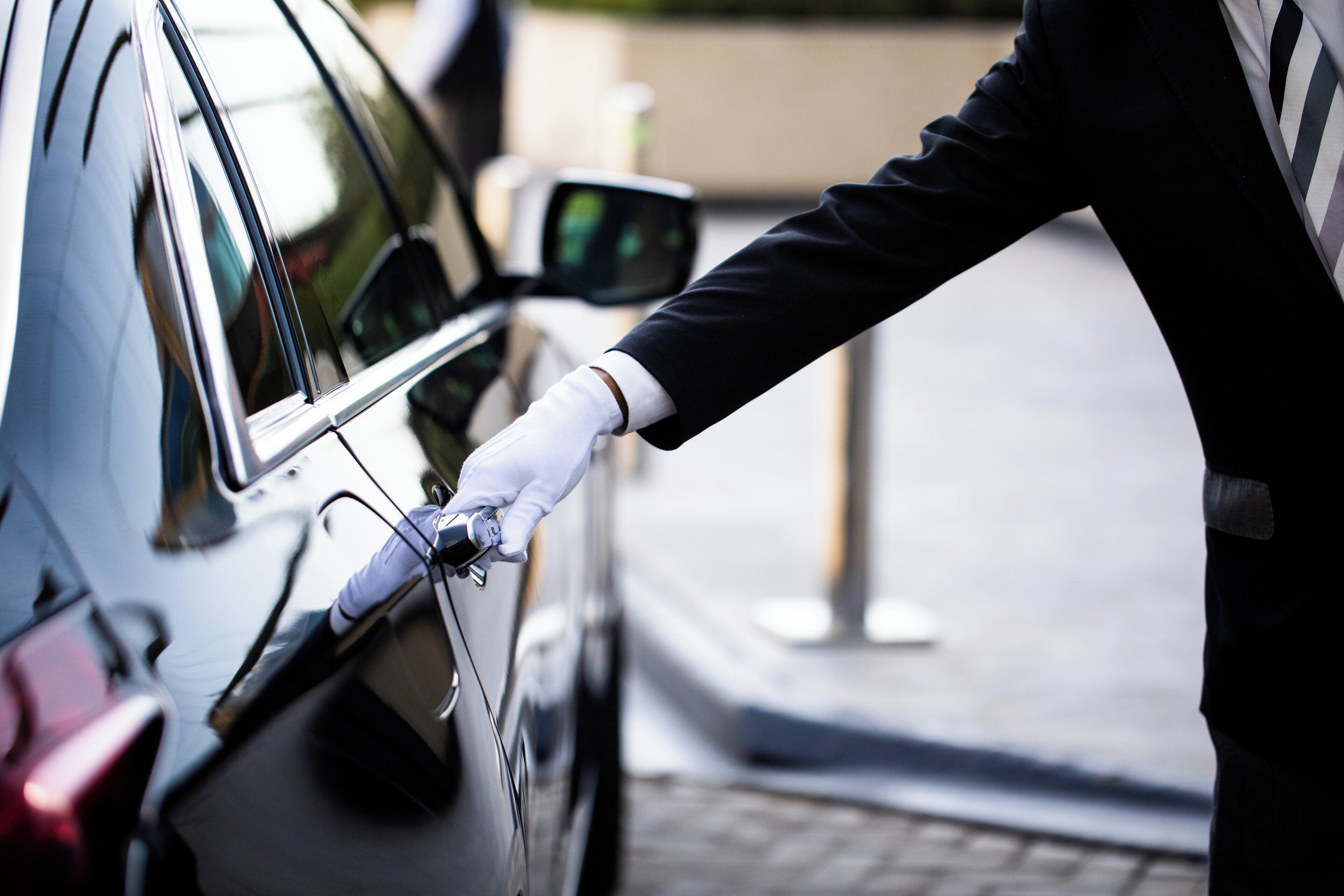 Une personne en costume et portant des gants ouvre la portière d’une voiture.