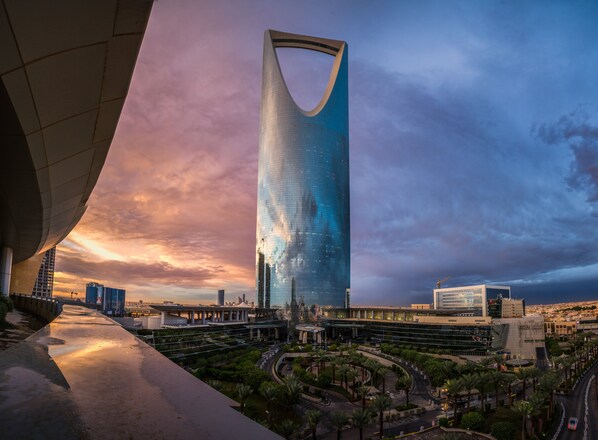 A modern skyscraper with a unique curved top, surrounded by a well-maintained urban area with roads and greenery.