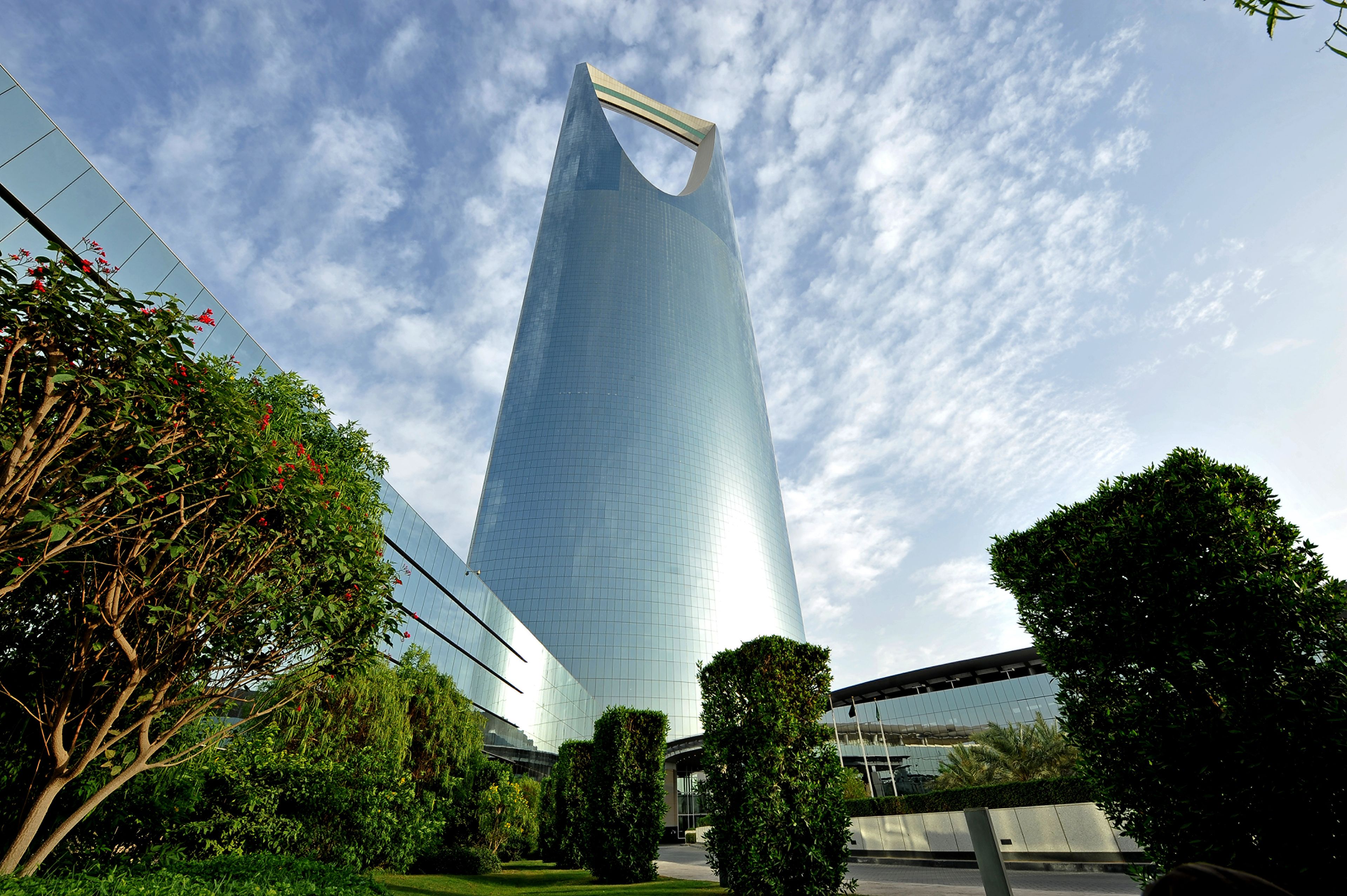 A modern skyscraper with a unique curved top, surrounded by well-maintained greenery and a clear sky.