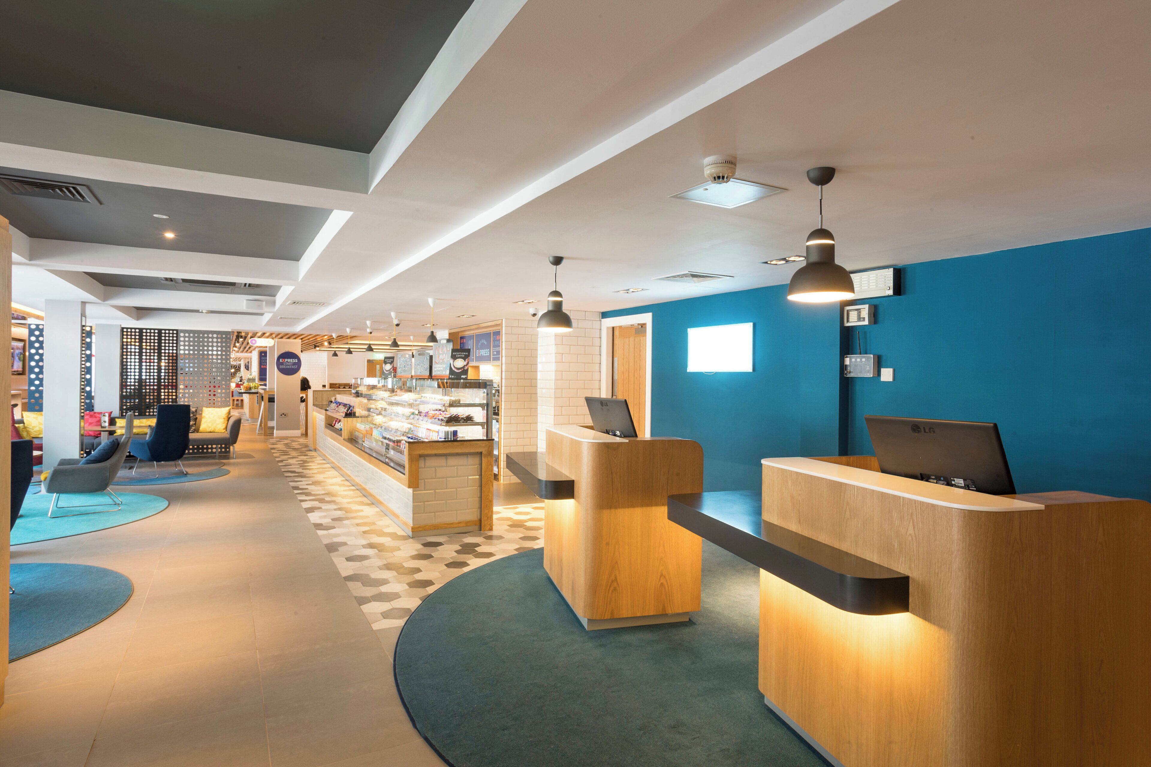 A modern hotel lobby with a reception desk, seating area, and a visible coffee shop.