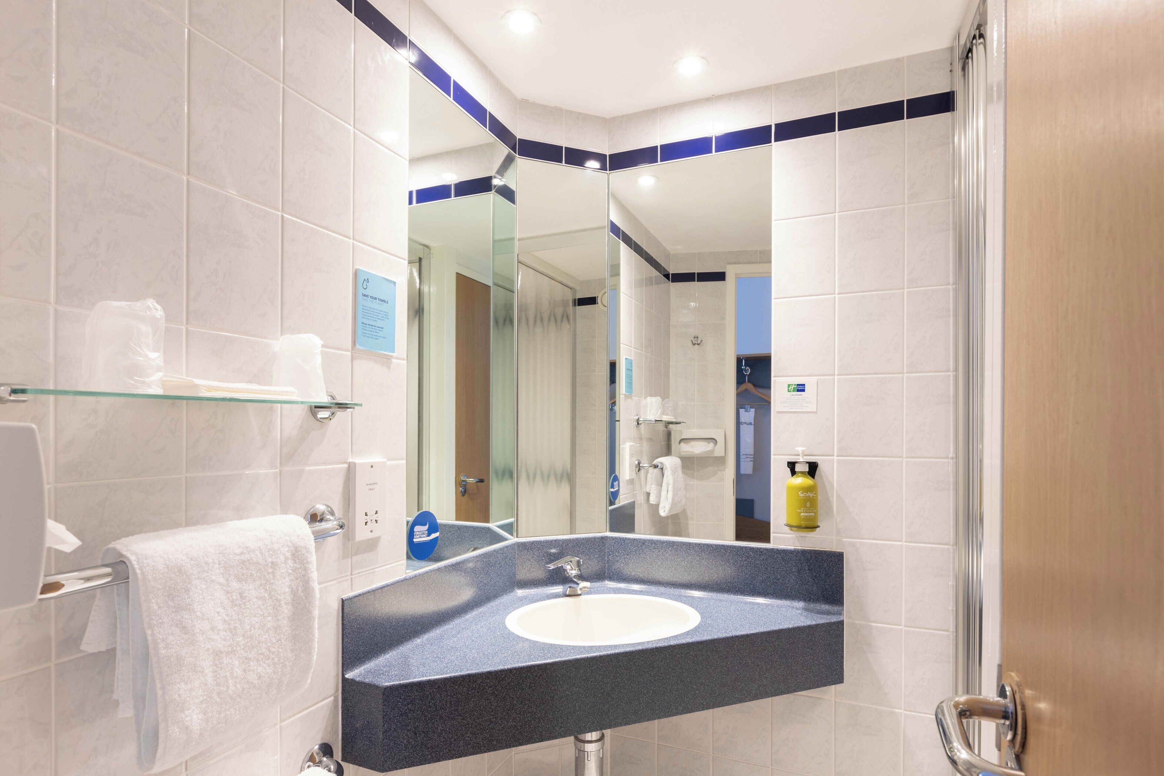 A modern bathroom with a glass shelf holding toiletries, a sink with a mirror above it, and a shower area visible through a glass door.