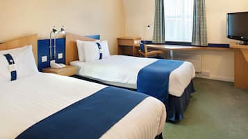 Habitación de hotel con dos camas, un escritorio, una silla, un televisor y una ventana con cortinas.