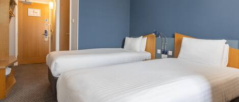 A hotel room with two beds, a wooden wardrobe, a door with a certificate, and a blue wall.