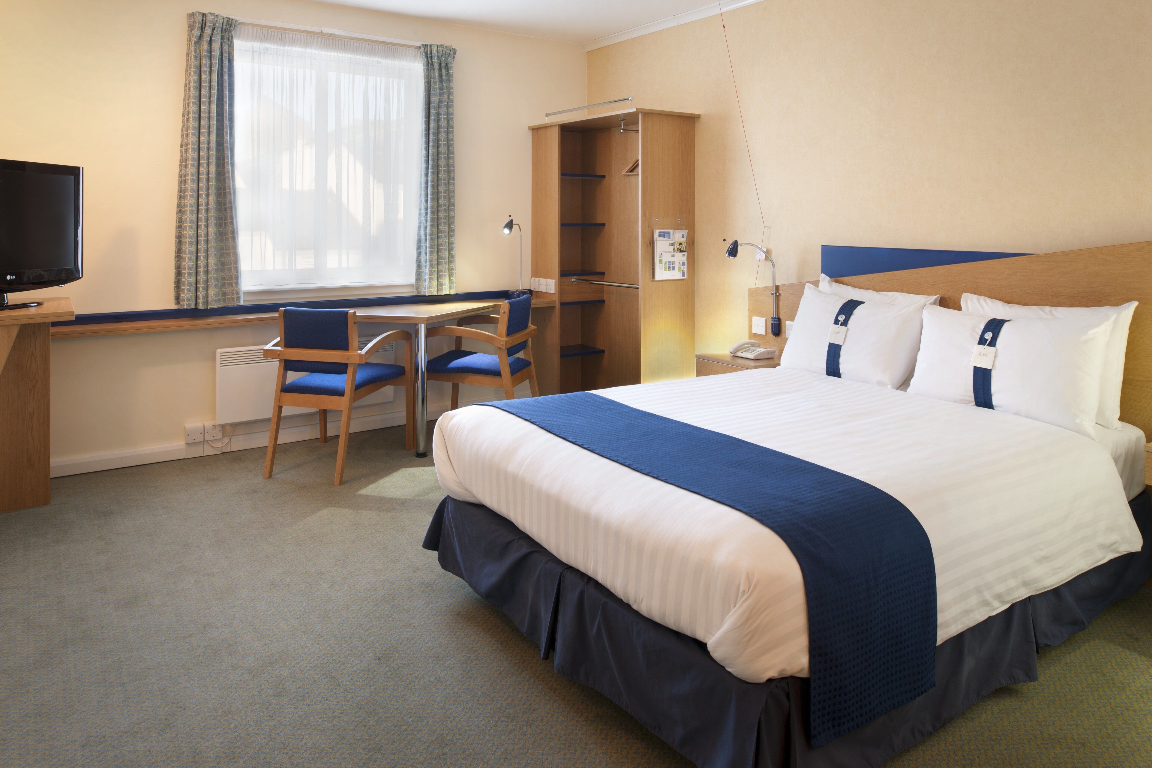 A hotel room with a bed, a desk with a chair, a television, and a wardrobe.