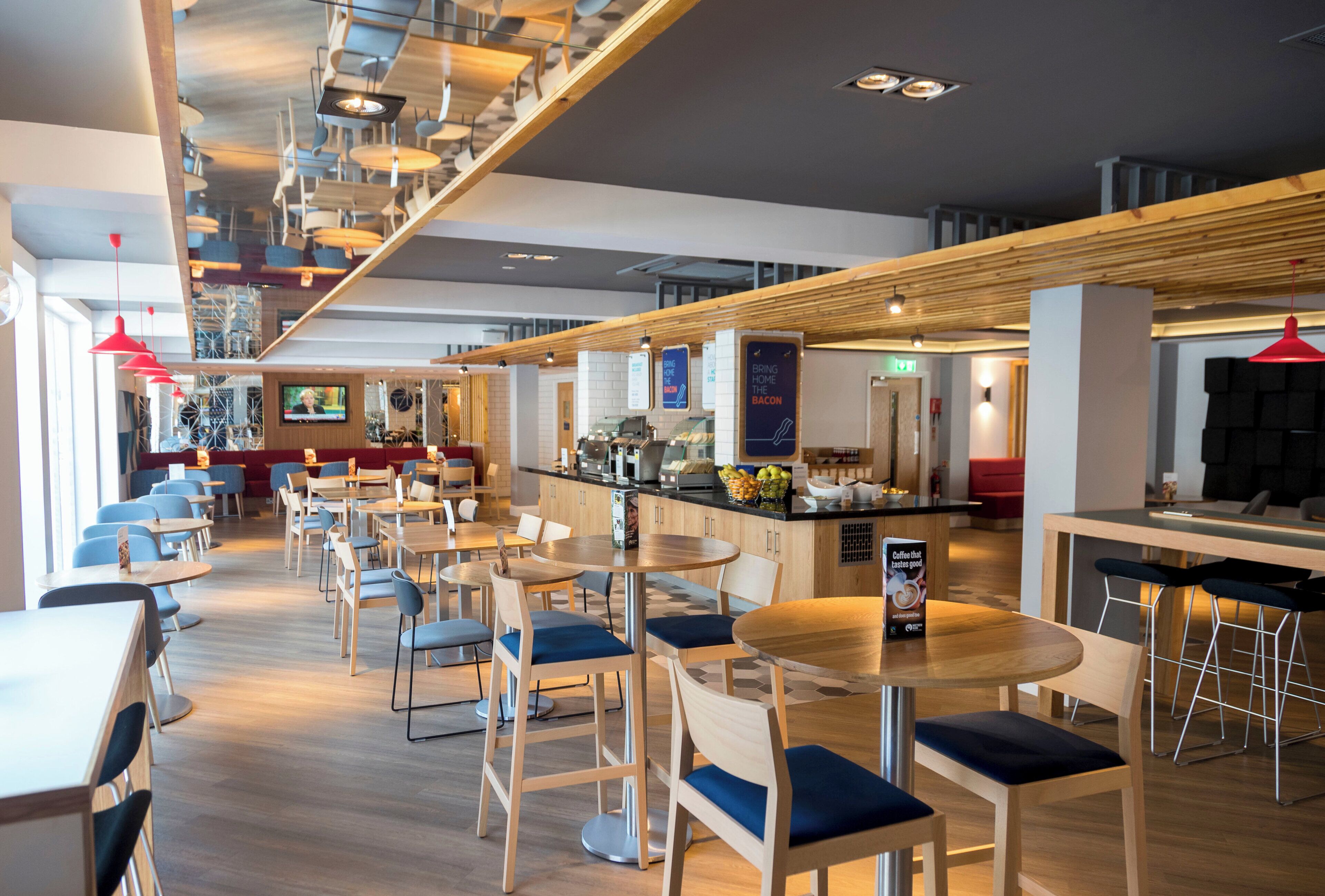 Un restaurant moderne doté de plusieurs espaces de restauration, comprenant des tables et des chaises, et dont la cuisine est visible.