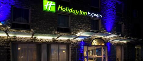 Edificio Holiday Inn Express con fachada de piedra, amplias ventanas y una entrada destacada con toldo.