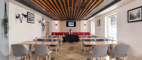 Una sala de conferencias con mesas y sillas de madera, un sofá rojo y una pantalla de televisión en la pared.