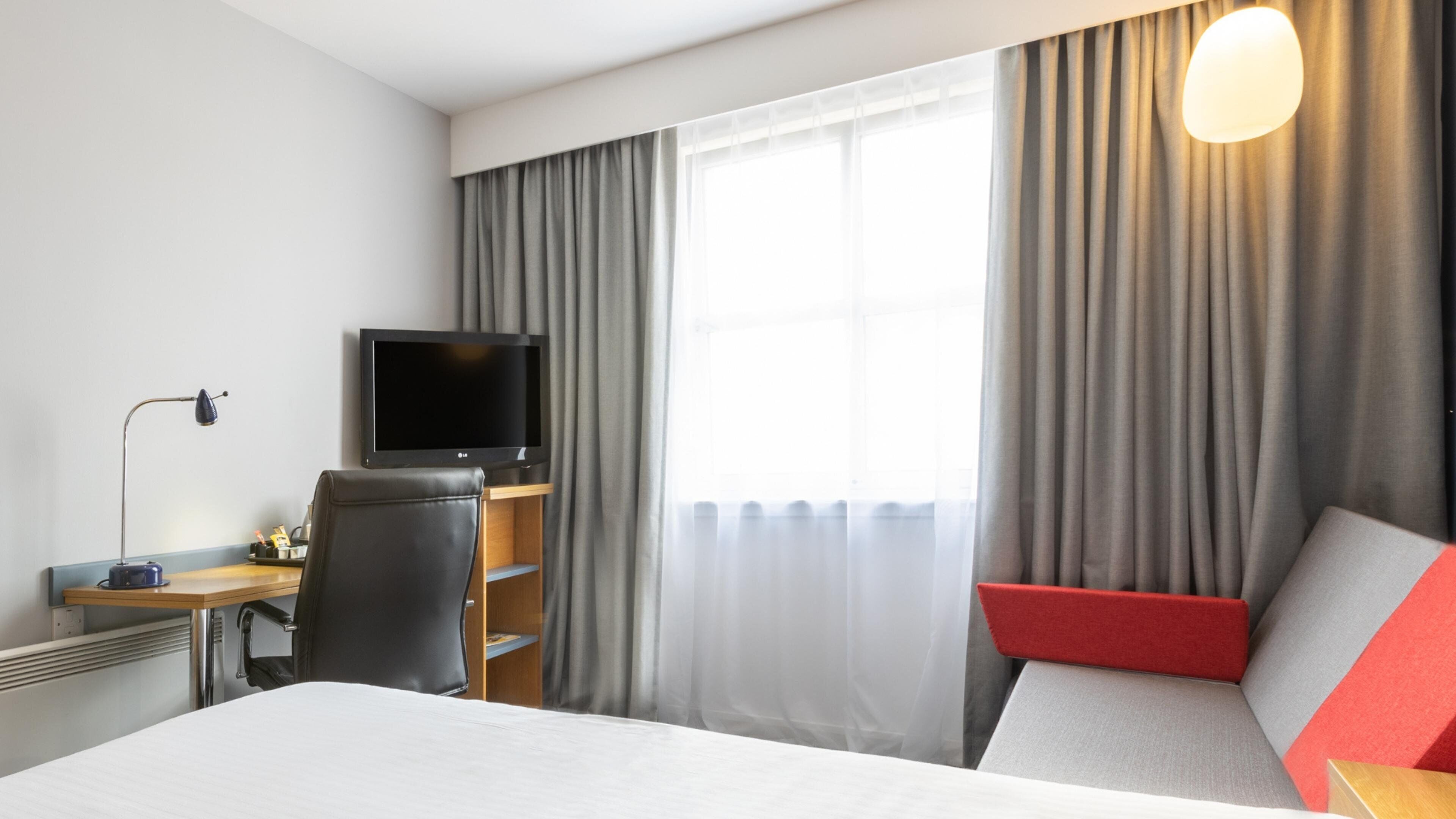 A hotel room with a bed, a desk, a chair, a television, and a window with curtains.