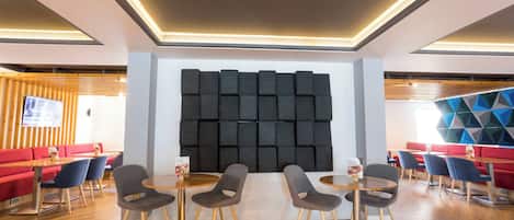 A modern interior with a central acoustic panel, wooden flooring, and a mix of red and blue seating.