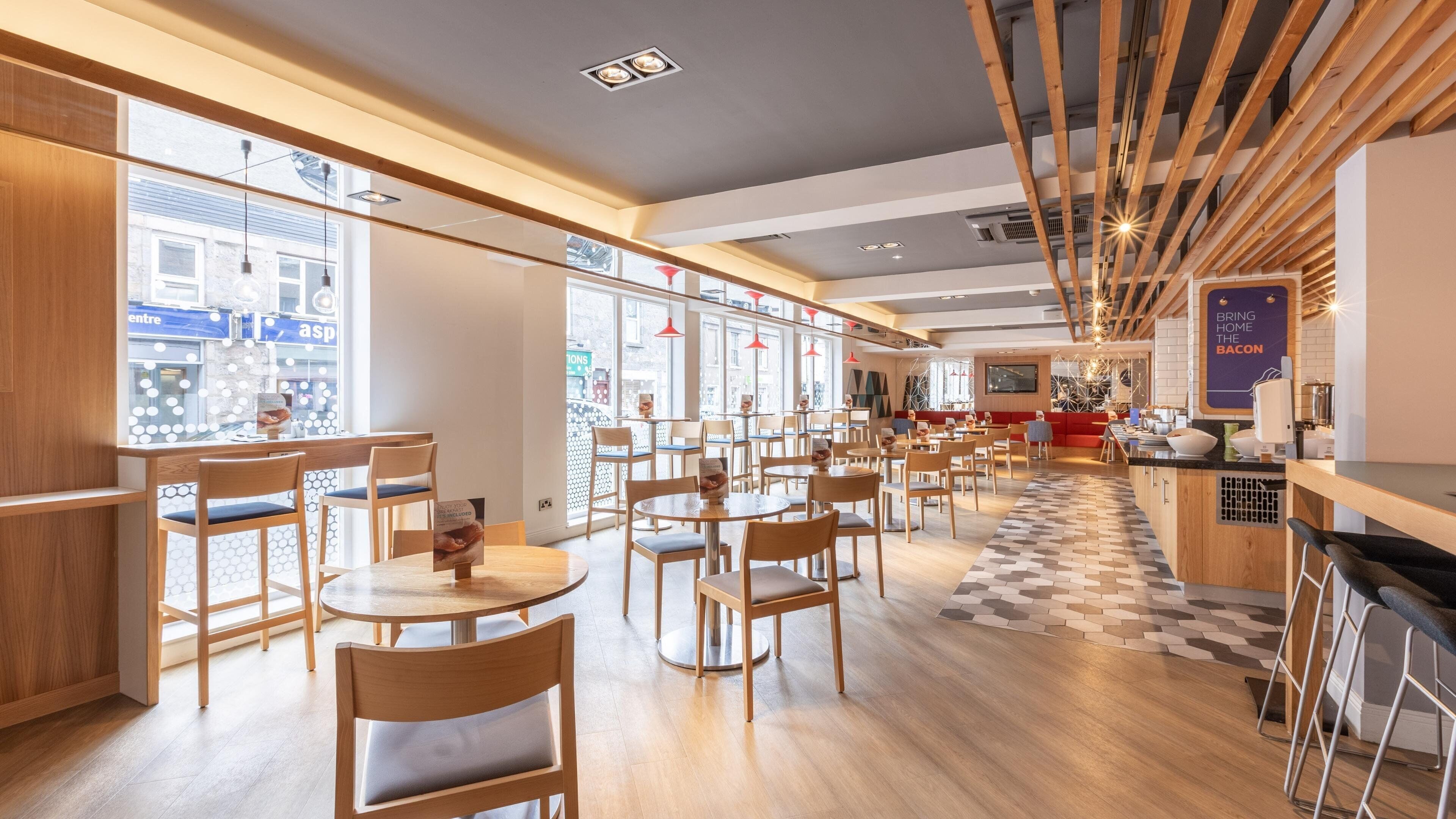 Un ristorante moderno con arredi in legno, ampie finestre e una zona bar centrale.