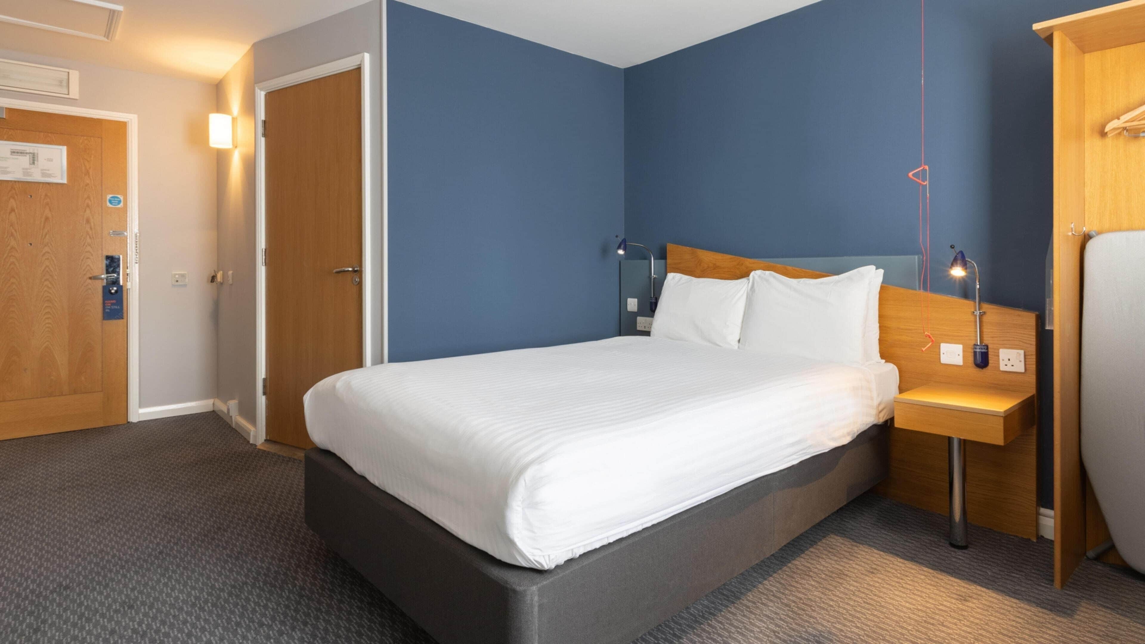 A hotel room with a bed, bedside table, lamp, and a wardrobe.