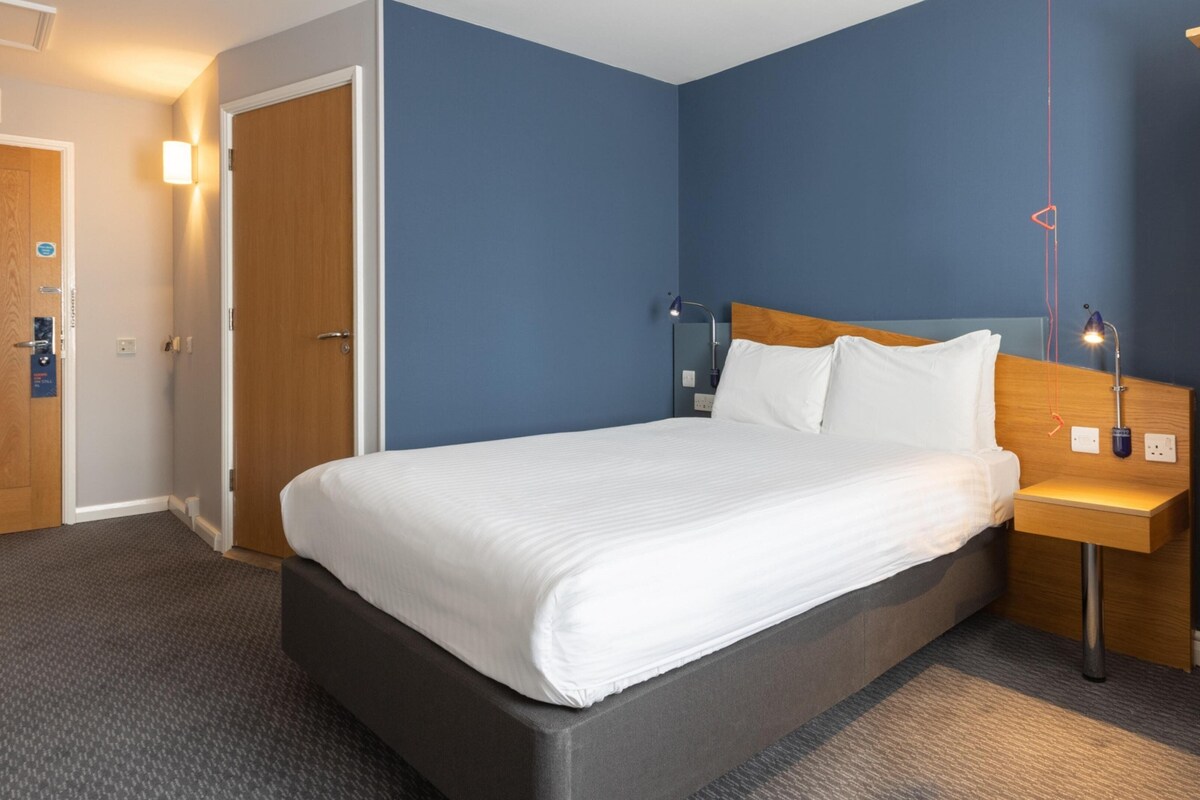 Et hotelværelse med seng, natbord, lampe og et klædeskab.
