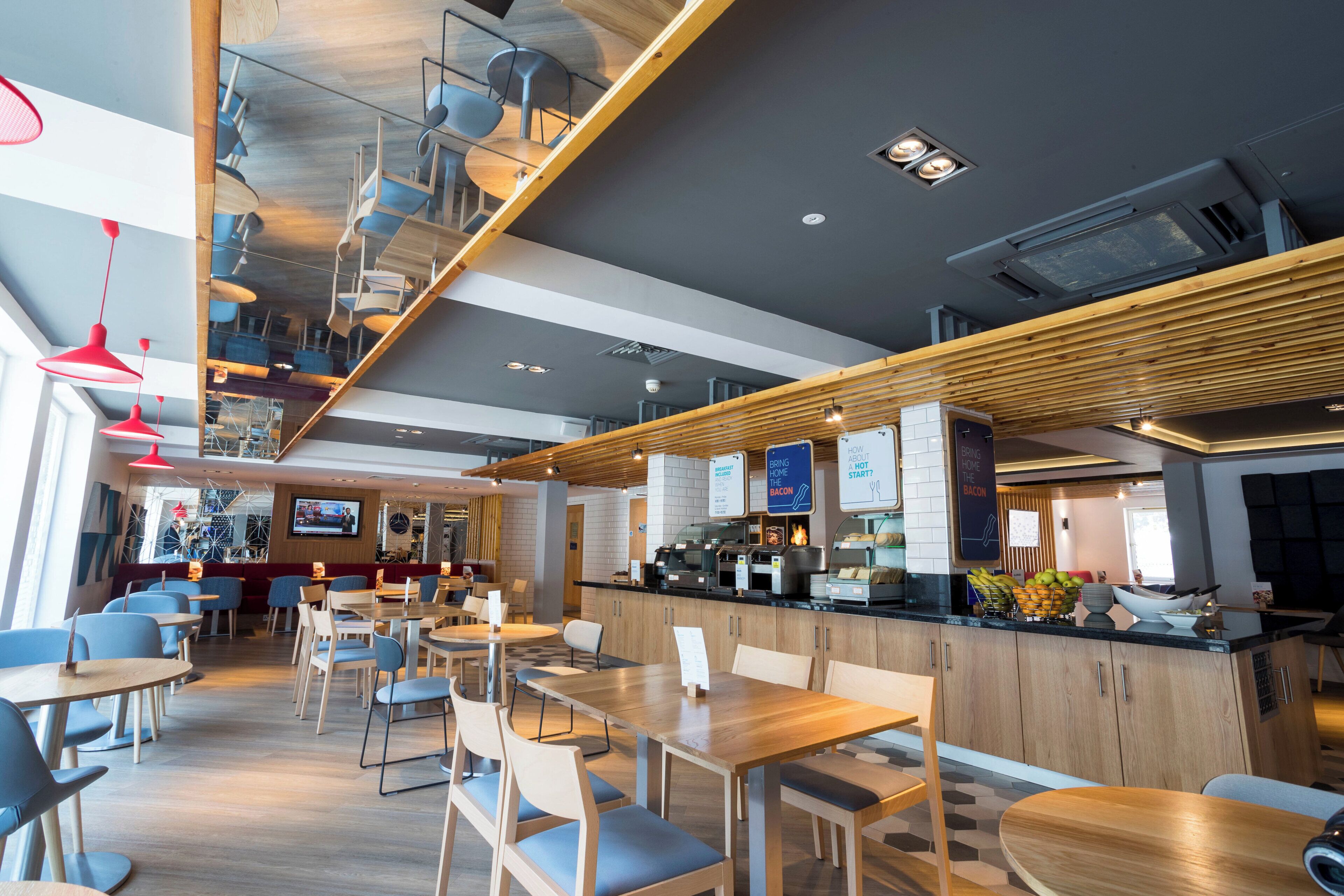 Interior modern d'un restaurant amb sostres alts, bigues de fusta i diverses opcions de seients, com ara taules i cadires.