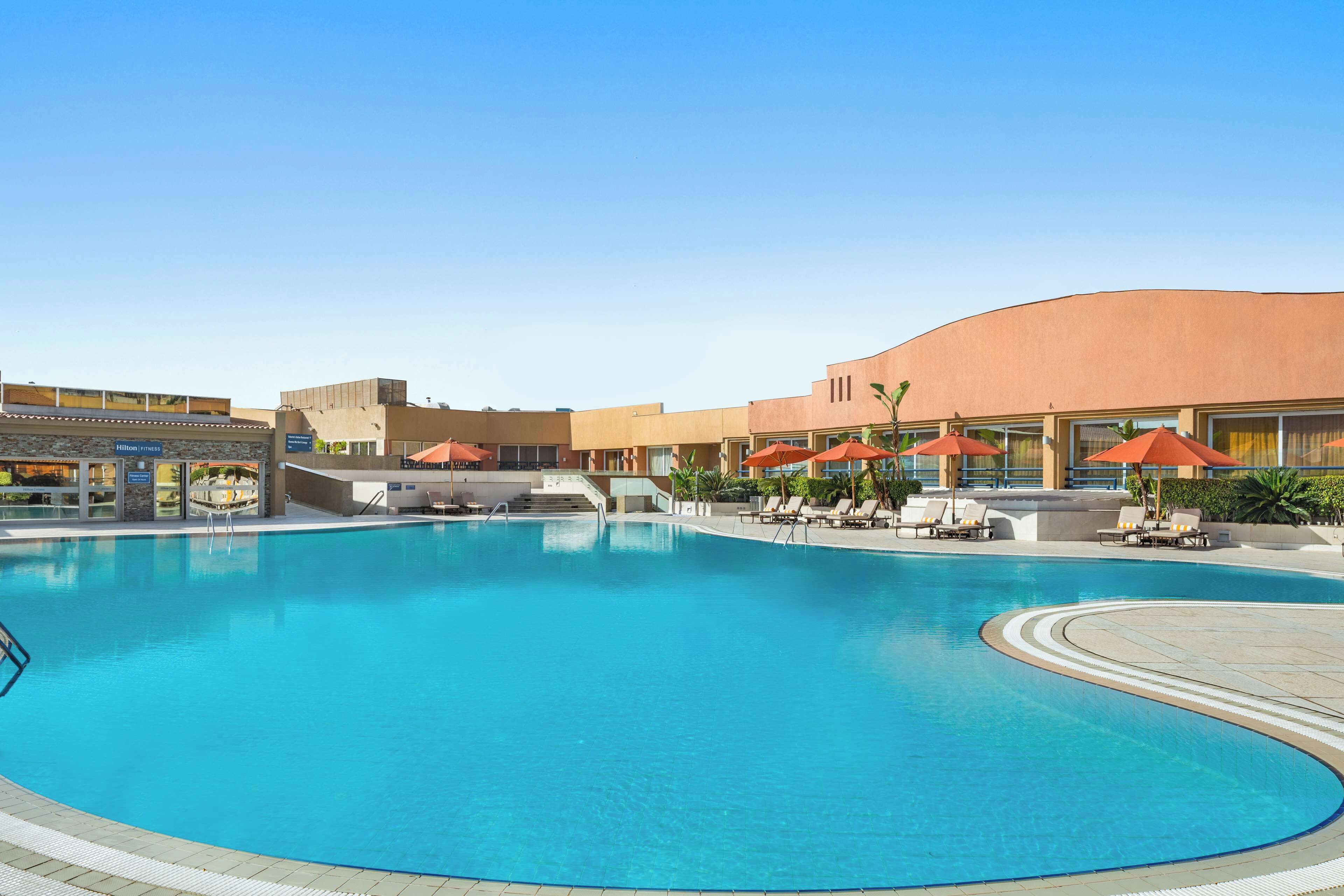 Una piscina con tumbonas y sombrillas, rodeada de edificios con fachada curva.