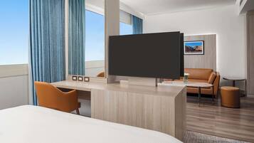 A modern hotel room with a large bed, a desk with a flat-screen TV, a leather sofa, and a small round table.