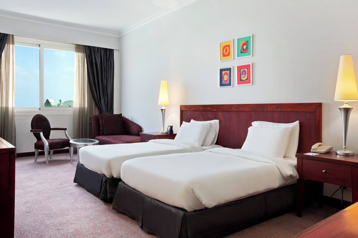 Habitación de hotel con dos camas, una silla, un escritorio y una lámpara.