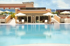 A swimming pool with lounge chairs and umbrellas, surrounded by a building with a tiled roof and stone walls.