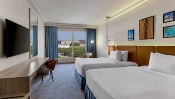 A hotel room with two beds, a desk, a chair, a TV, and a large window with a view.