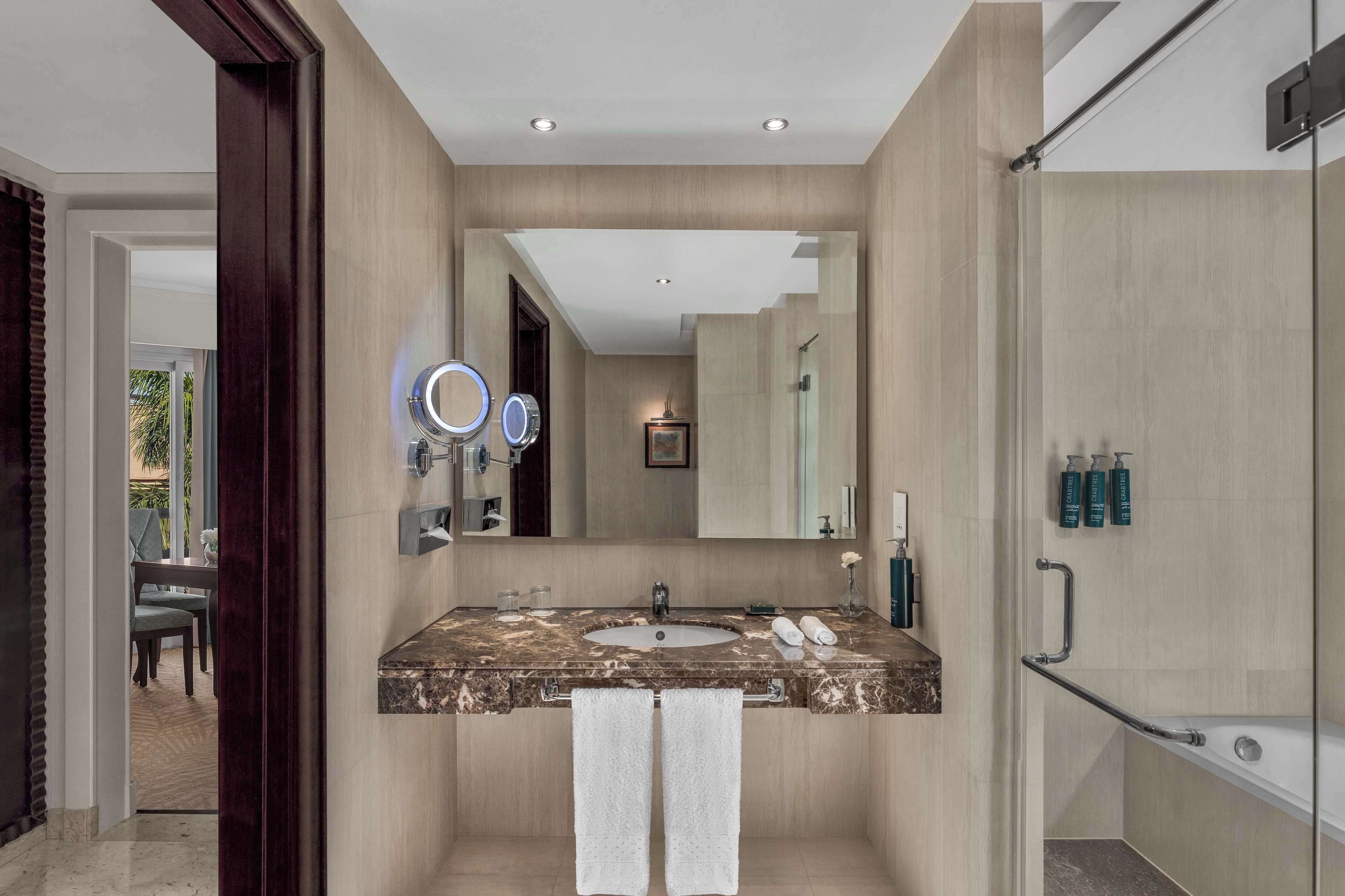 A modern bathroom with a marble sink, two towels, a large mirror, and a glass-enclosed shower.