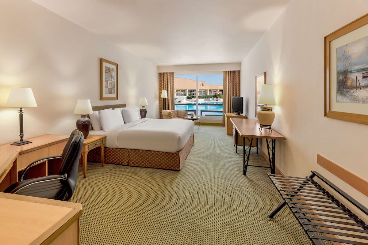 Habitación de hotel con cama, escritorio, silla y vista a una piscina.