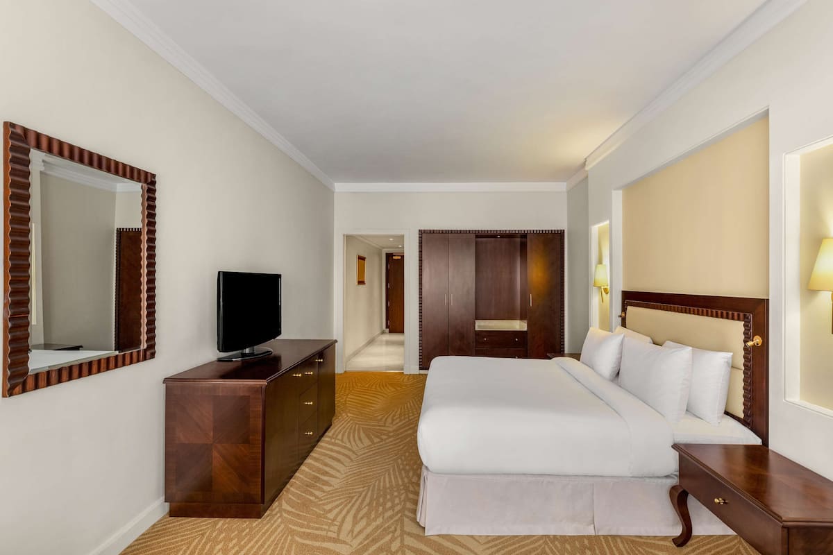 Una habitación de hotel con una cama grande, televisión, cómoda de madera y espejo.