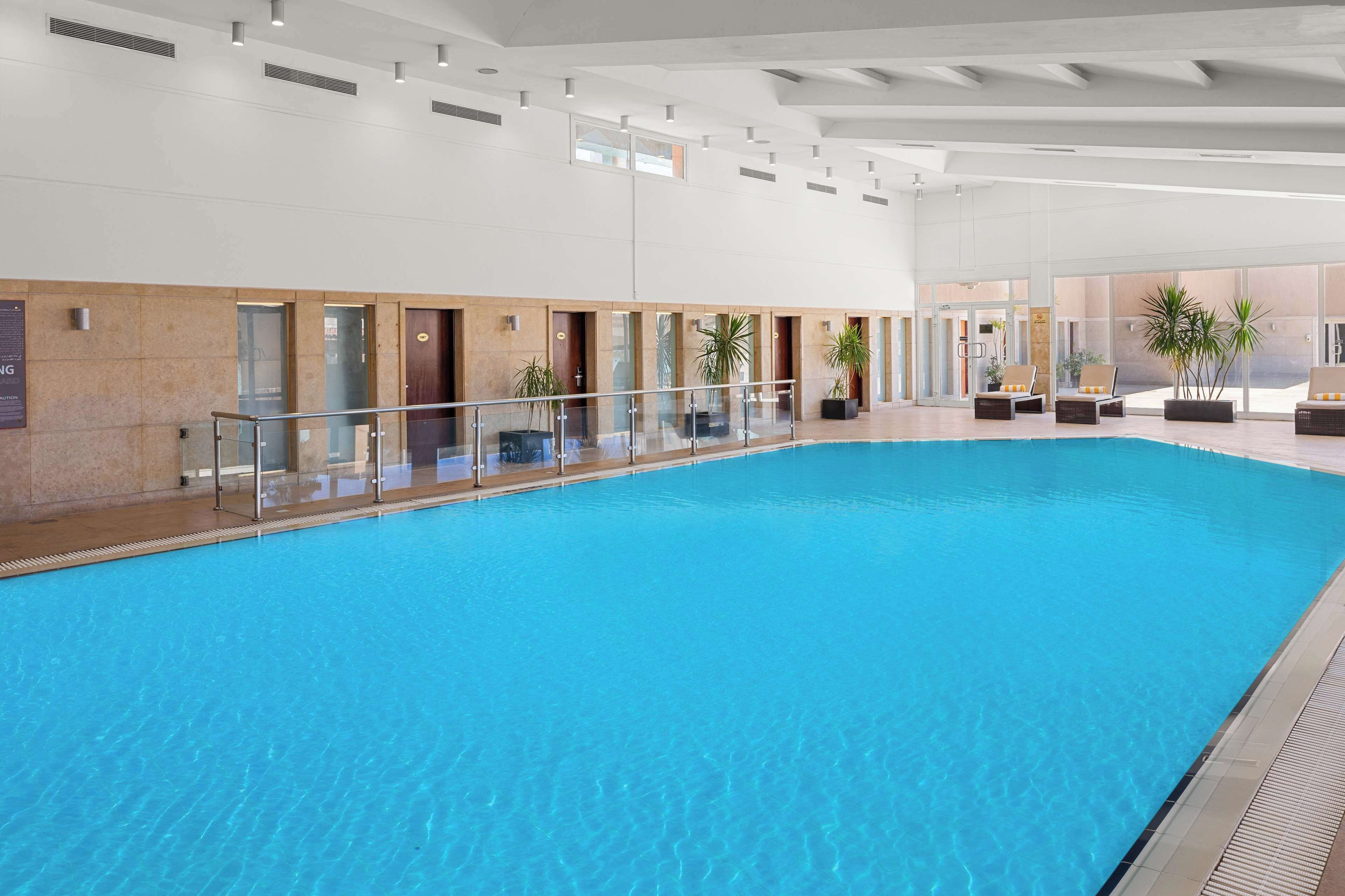 Una amplia piscina interior con agua cristalina, rodeada de barandillas de vidrio y plantas en macetas.