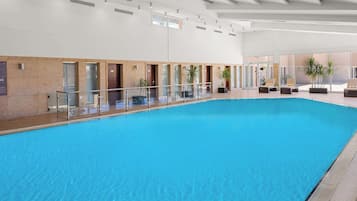 Una amplia piscina interior con agua cristalina, rodeada de barandillas de vidrio y plantas en macetas.