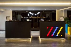 A hotel reception desk with a neon sign reading 'Roomzz' and a welcome sign for Nottingham City. - Roomzzz Nottingham City (Nottingham)