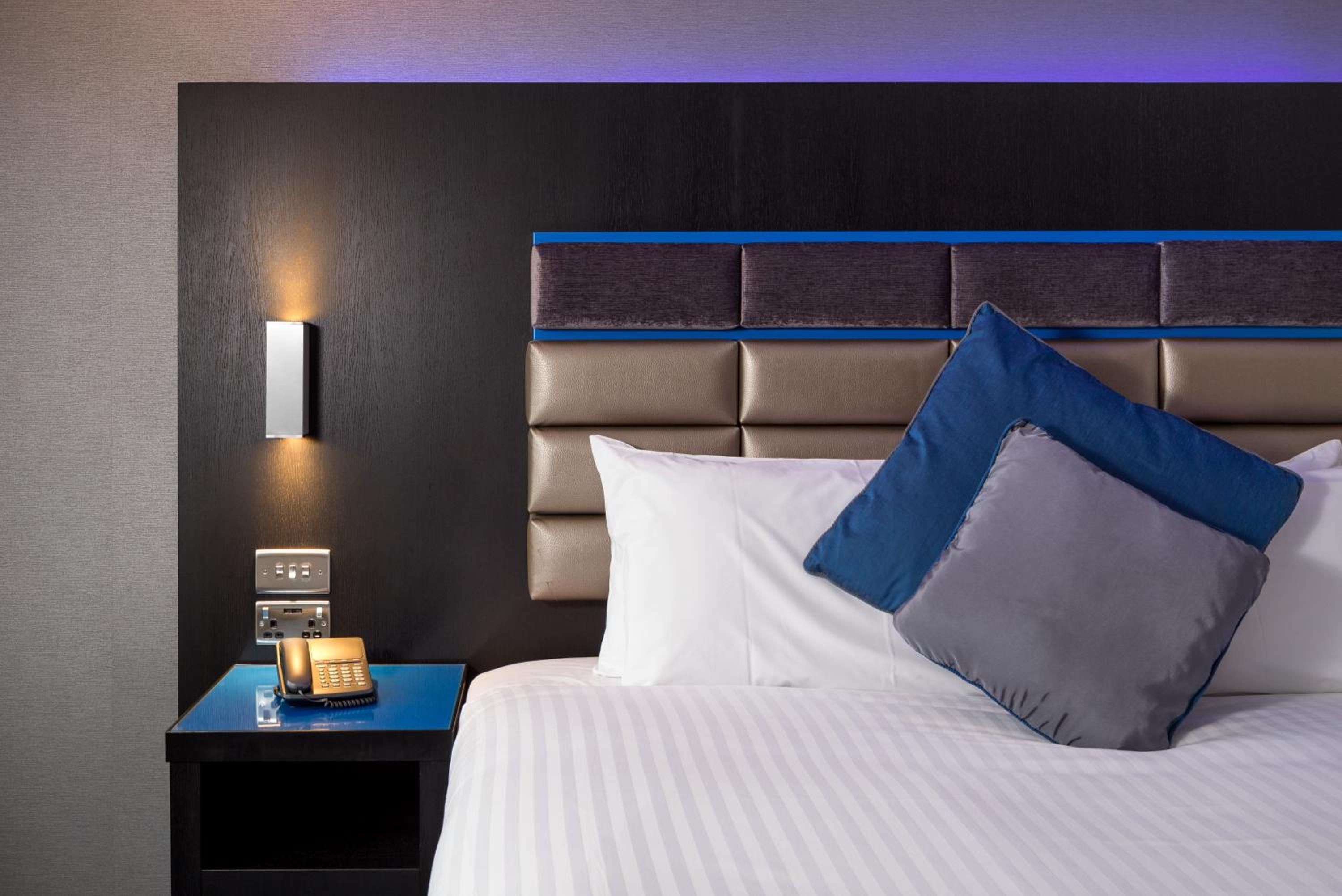 Une chambre d’hôtel avec un lit, une table de chevet avec un téléphone et une lampe fixée au mur.