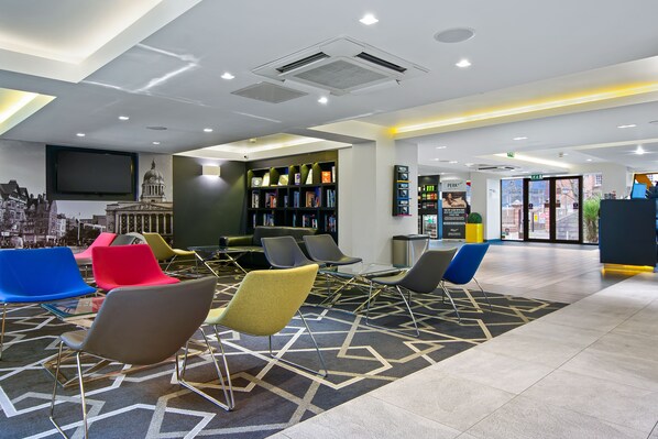 A modern lobby with colorful chairs, a large bookshelf, and a flat-screen TV.