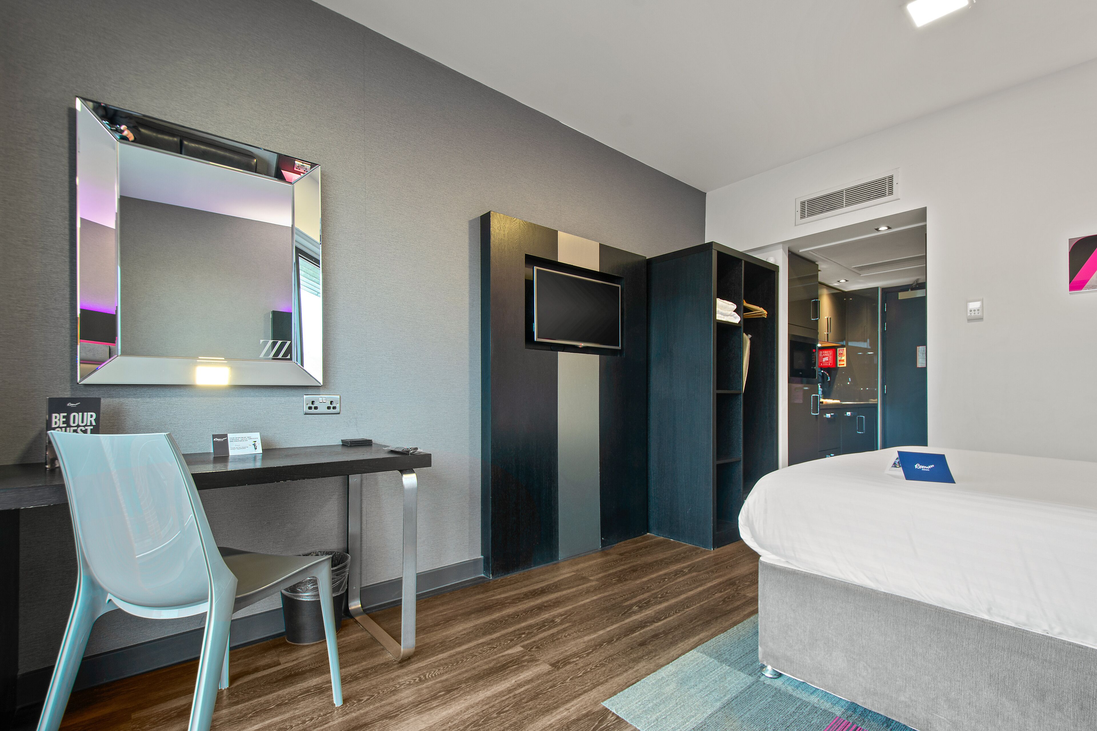 Una habitación de hotel moderna con escritorio, silla, cama y un espejo grande.