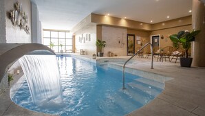 An indoor swimming pool with a waterfall feature, surrounded by seating areas and potted plants. - Eden Hôtel & Spa Cannes (Cannes)