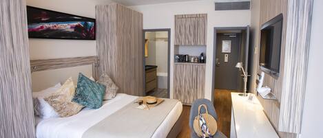 A modern hotel room with a bed, a desk, a chair, a TV, and a painting on the wall.
