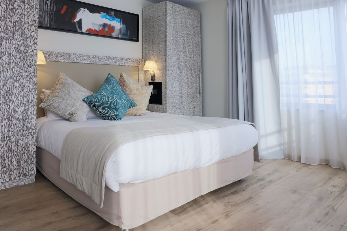 Une chambre à coucher moderne avec un grand lit, une lampe fixée au mur et un tableau au-dessus du lit.