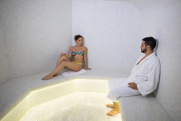 Dos personas sentadas en un cuarto con azulejos y una piscina pequeña.