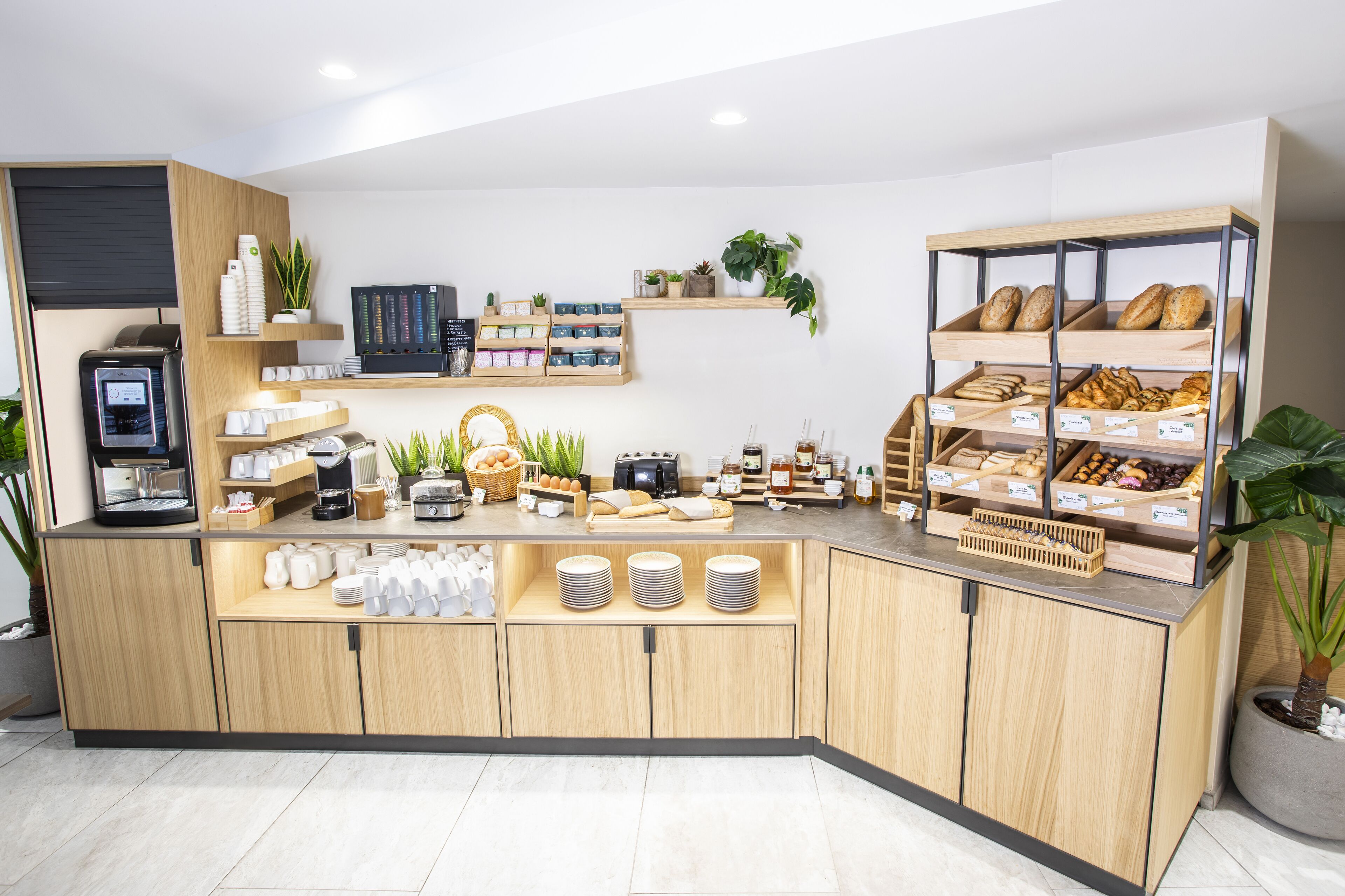 A breakfast bar with various food items, coffee machines, and decorative plants.