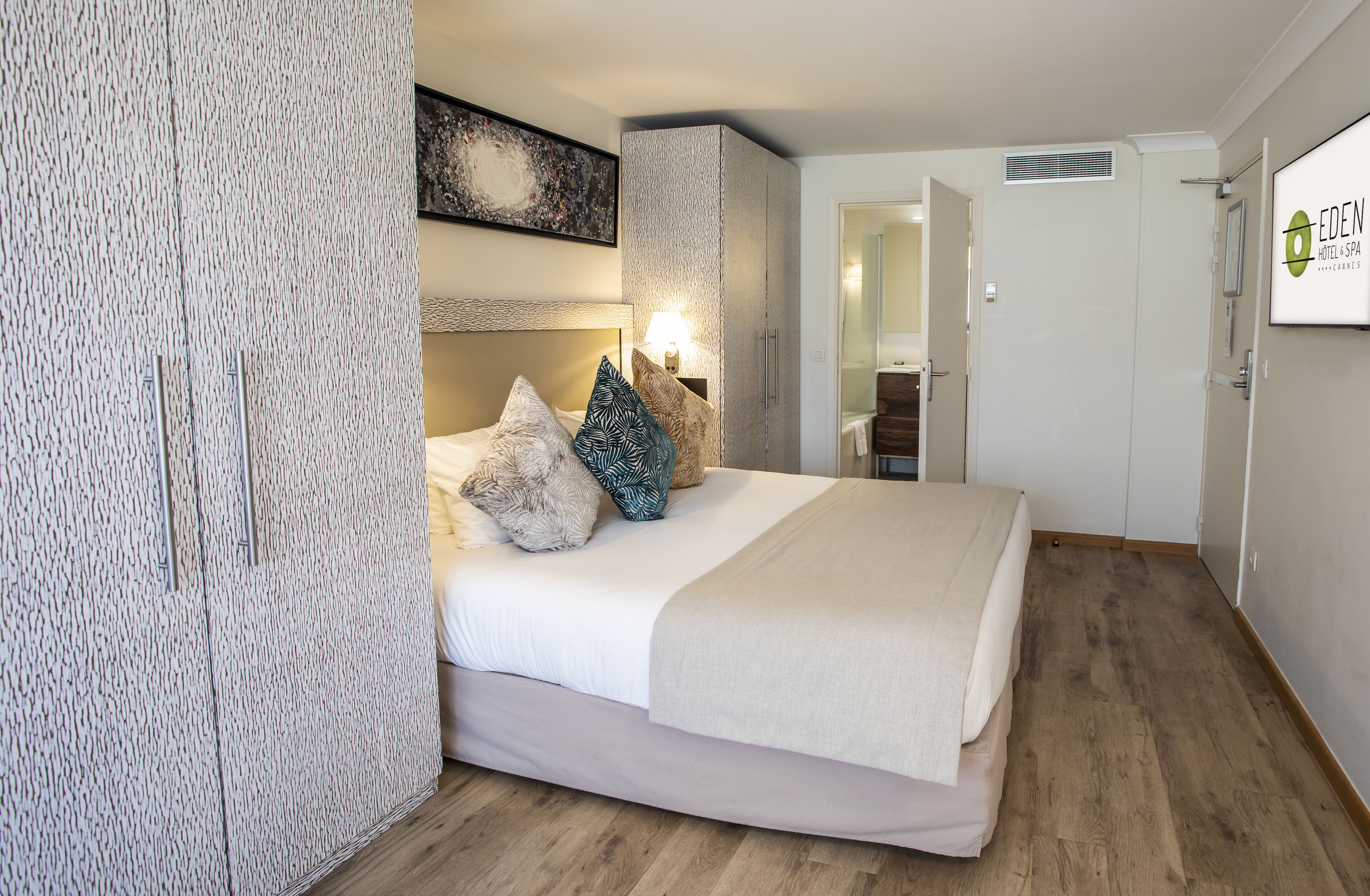 Una habitación de hotel con una cama, un armario, un espejo y una puerta al baño.