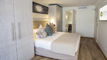 Una habitación de hotel con una cama, un armario, un espejo y una puerta al baño.