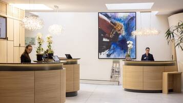 A modern reception area with two wooden reception desks, a large abstract painting on the wall, and hanging pendant lights.